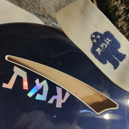 top part of the front of the ric with the word, "אמת," in rainbow holographic vinyl and part of the guitar strap showing a classic golem shape embroidered on it.